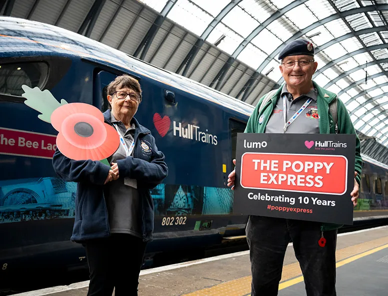 2 people standing on the platform by a Hull Trains service with a Poppy Express banner