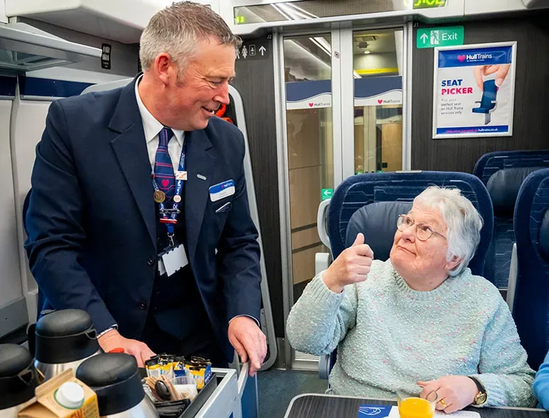 A photo of the Hull Trains onboard host serving cold drinks to two passengers